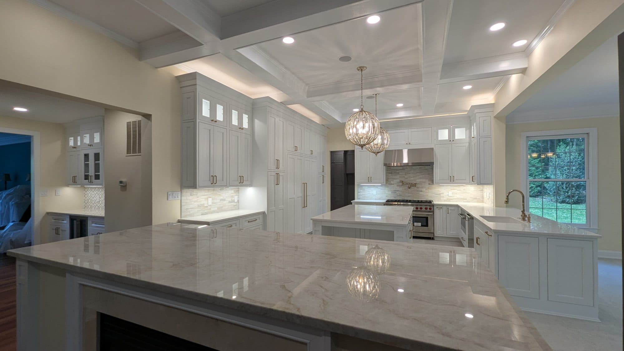 Renovated kitchen with a large waterfall-edge island, gold hardware, and coffered ceiling