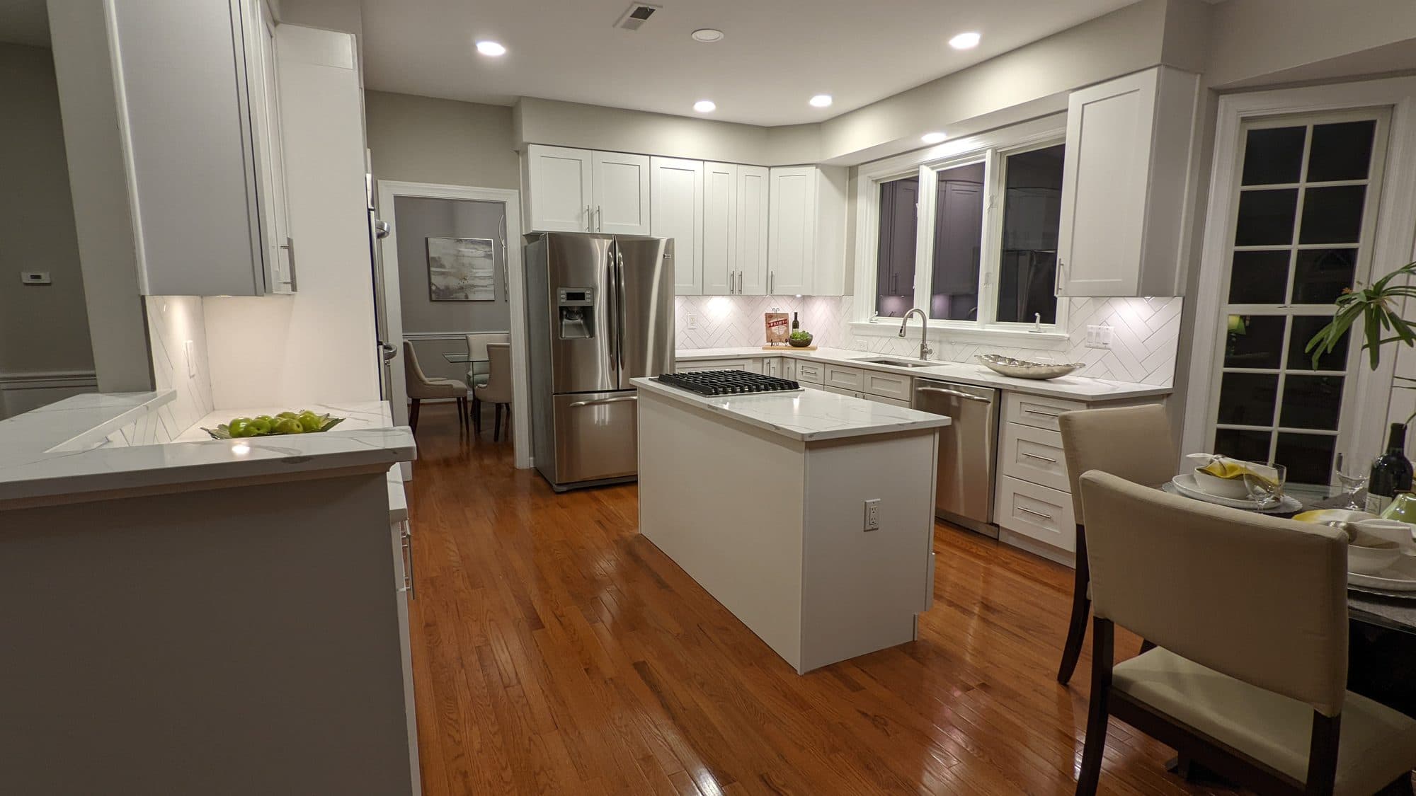 Kitchen island with a gas cooktop and integrated dishwasher, herringbone backsplash in the background